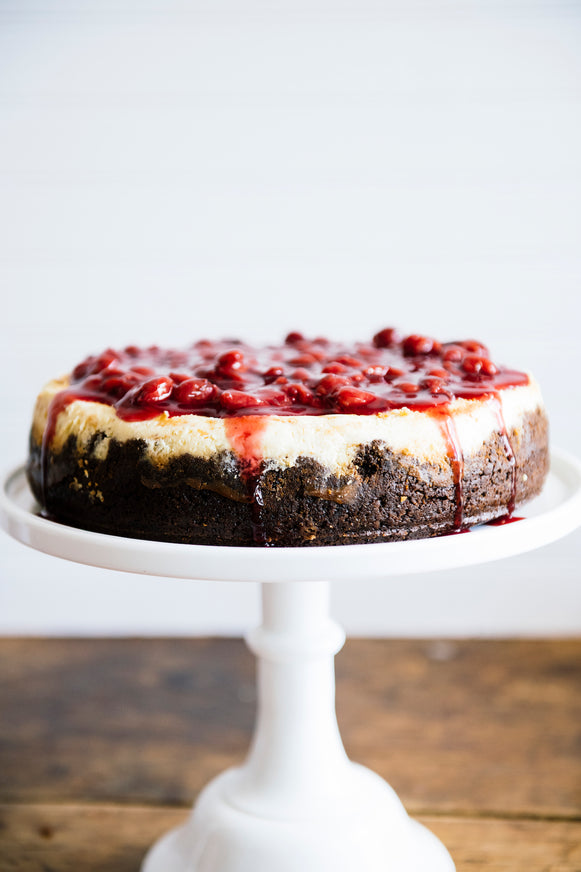 A homemade cheesecake on a cake stand topped with sour cherries