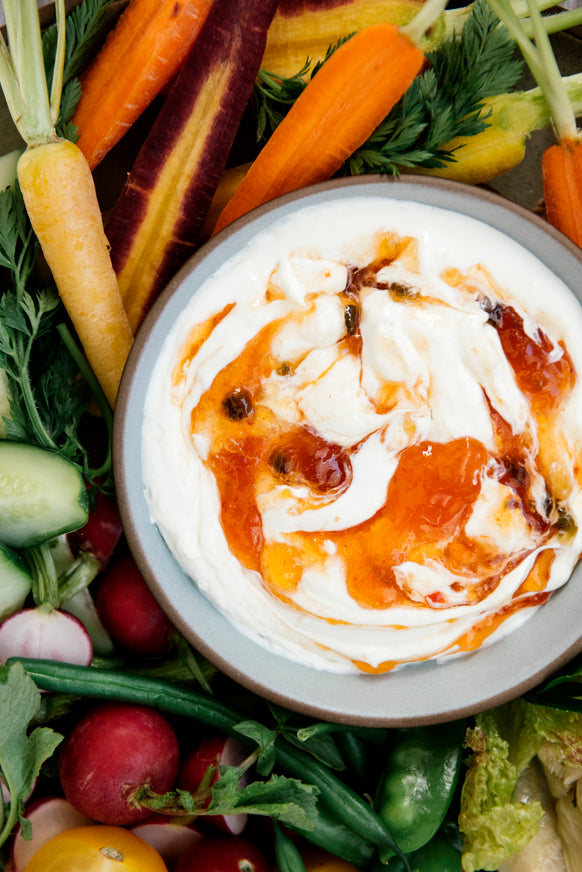 a tray of freshly cut vegetables with a dip topped with pepper jelly