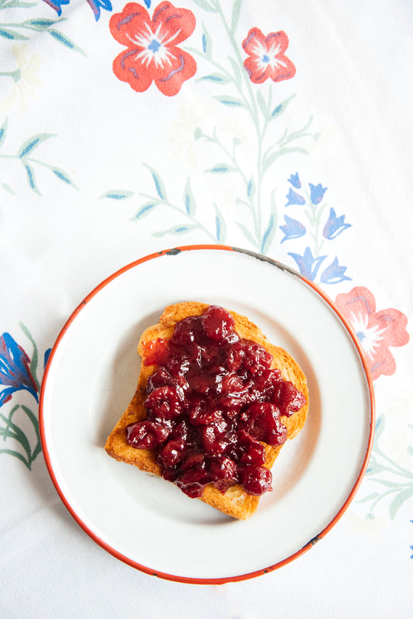A slice of toast topped with sour cherry preserves on a floral table cloth