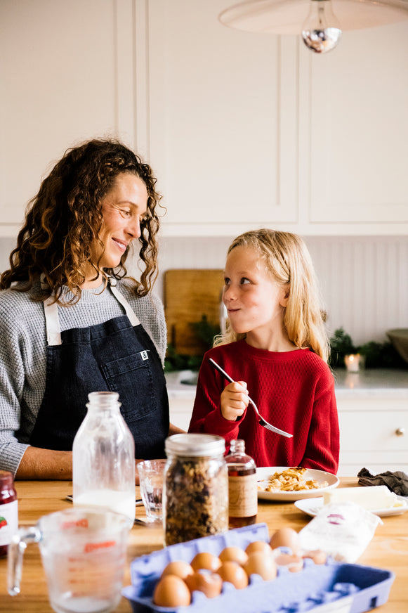 A mother and daughter eating pancakes together with the ingredients across the kitchen island.