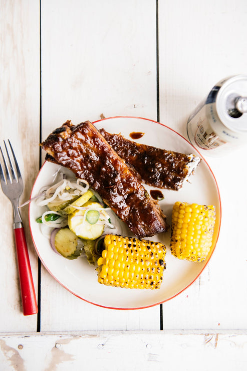 Load image into Gallery viewer, a plate of ribs, pickles, slaw and corn