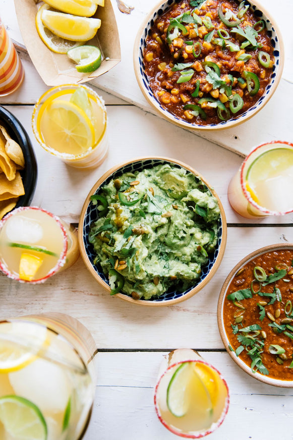 bowls of guacamole, chips, salsa, bean dip, street corn dip and glasses of margaritas