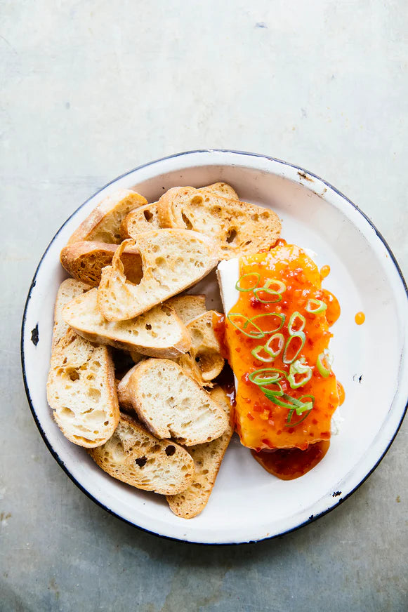 slices of baguette next to a block of cream cheese topped with jalapeno pepper jelly