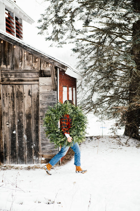 Load image into Gallery viewer, a woman walking across a yard carrying a wreath in front of a barn