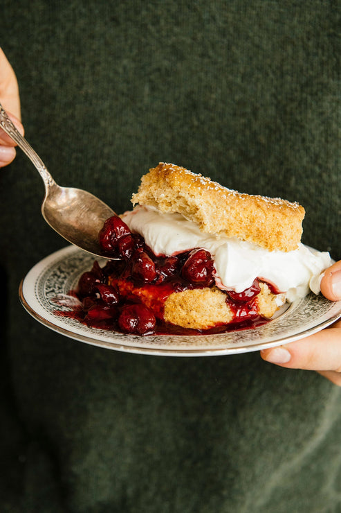 Load image into Gallery viewer, a person in a green sweater eating cherries and whipped cream on a biscuit