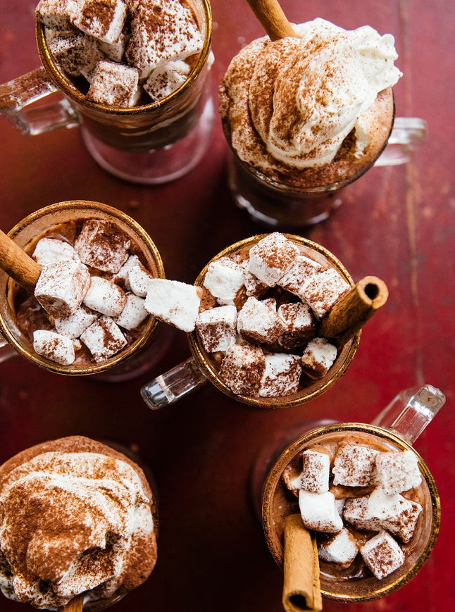 six mugs of hot cocoa with marshmallows and whipped cream on a red background