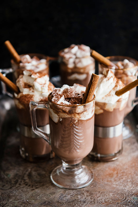 mugs of hot cocoa topped with marshmallows, whipped cream, cinnamon and cinnamon sticks