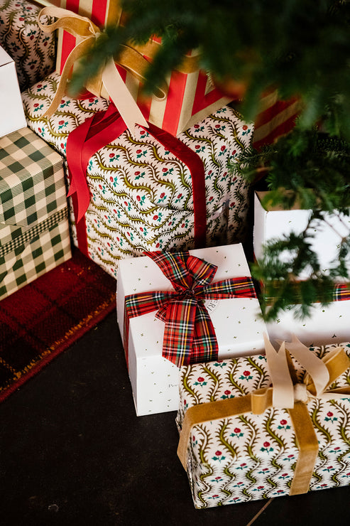 Load image into Gallery viewer, A collection of Christmas wrapped gift boxes under a tree, featuring festive patterns including green and white gingham, white with red and green botanical motifs, and plaid accents, tied with red, gold, and white ribbons.