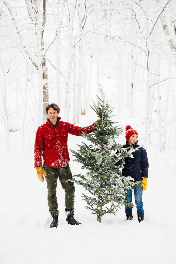 a dad and his son holding a cut down christmas tree in the snow