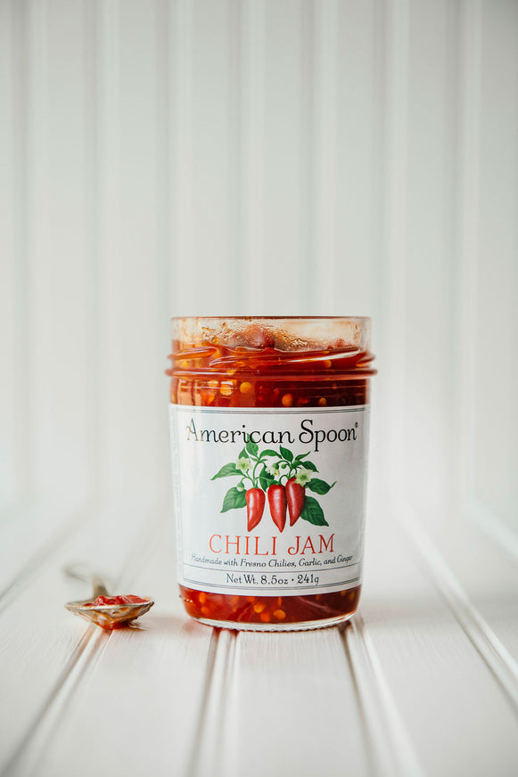 an open jar of chili jam next to a spoon topped with chili jam