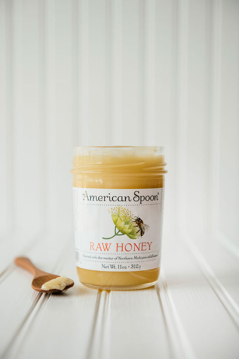 Load image into Gallery viewer, an open jar of raw honey with some honey on a wooden spoon set next to the jar