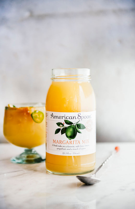 an open jar of Margarita Mix in front of a glass with a homemade margarita topped with jalapenos
