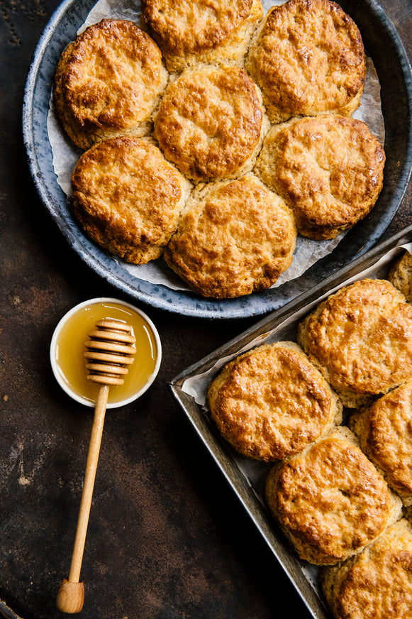 two pans of biscuits with a small bowl of honey