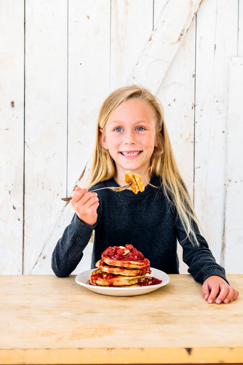 Load image into Gallery viewer, a little girl eating a stack of pancakes topped with fruit perfect sour cherries