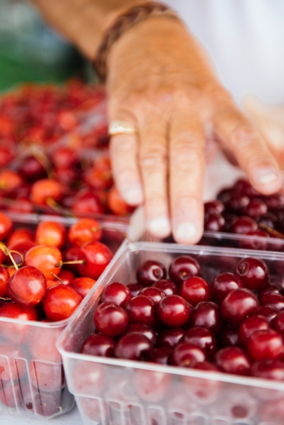 someone selecting baskets of farm market cherries