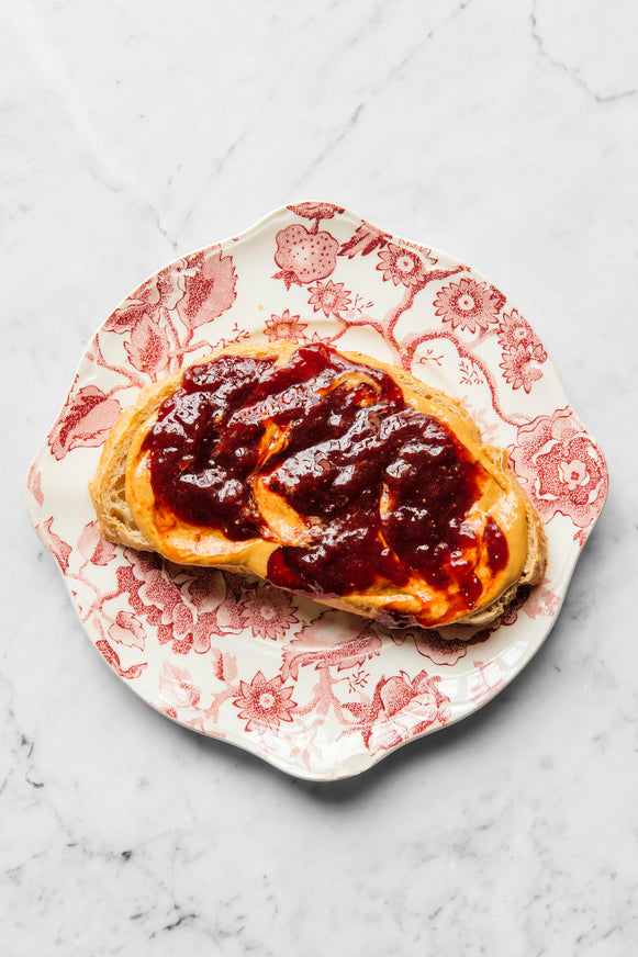 A piece of toast on a plate topped with peanut butter and jam