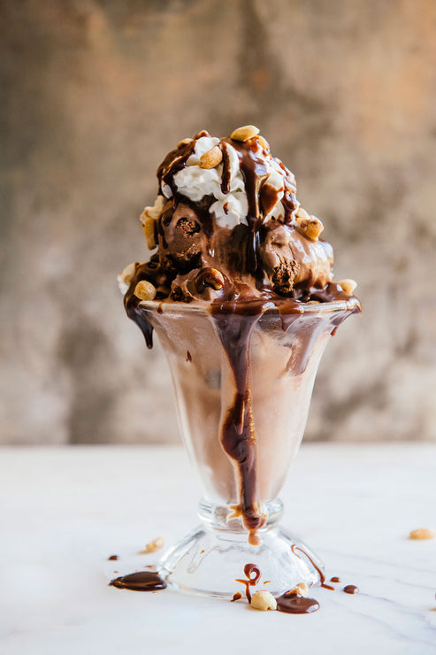 Load image into Gallery viewer, Chocolate ice cream sundae with nuts & whipped cream in a glass cup on a white surface.