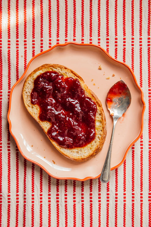 Load image into Gallery viewer, Toast with strawberry preserves on a pink plate with a spoon, all on a red and white striped tablecloth.