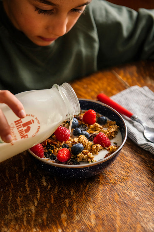 Load image into Gallery viewer, Person pouring milk into a bowl of Maple Granolas with berries on a wooden table