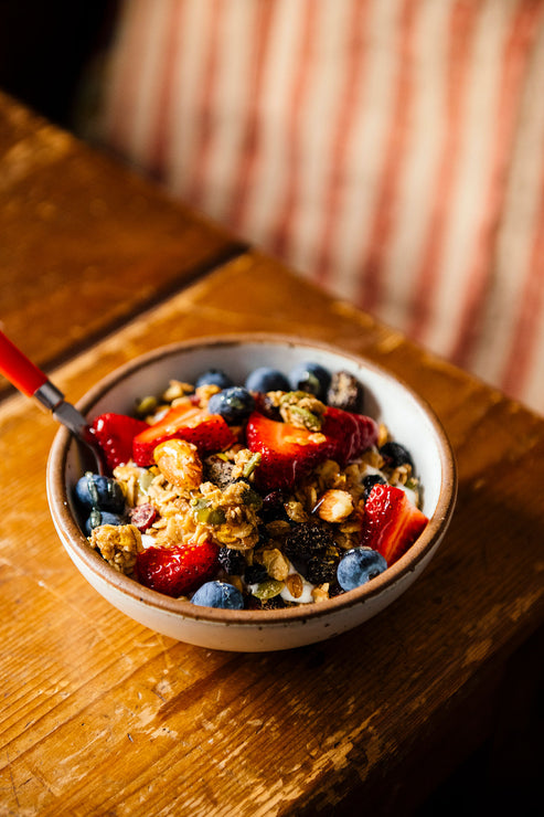 Load image into Gallery viewer, a bowl of maple granola topped with fresh fruit and honey