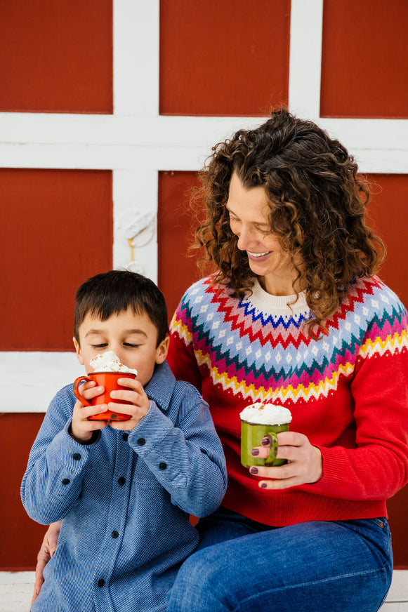 a mom and son drinking cups of hot cocoa with whipped cream