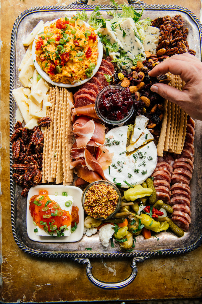 A charcuterie board with hands reaching in to select cheese, sausages.