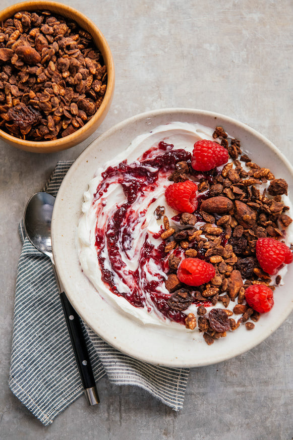 a bowl of yogurt topped with chocolate granola, fresh fruit and preserves