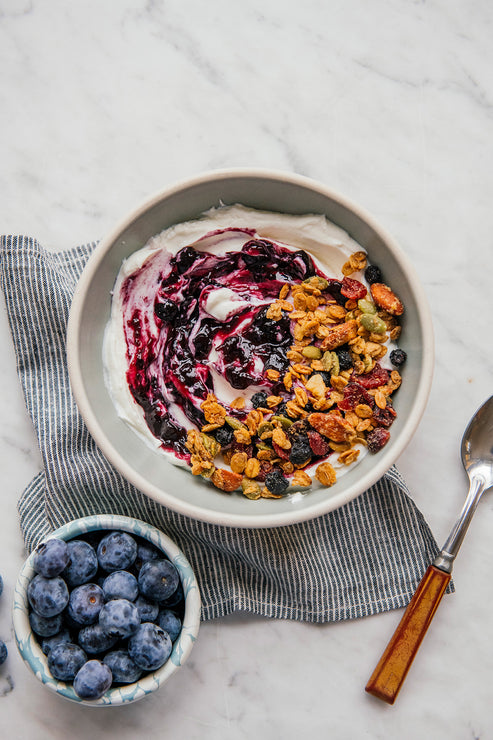 Load image into Gallery viewer, a bowl of yogurt and granola topped with blueberry preserves next to a small bowl of blueberries