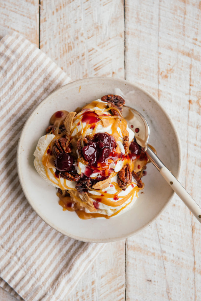 Overhead shot of a scoop of vanilla ice cream drizzled with caramel sauce, plus pecans and cherries.