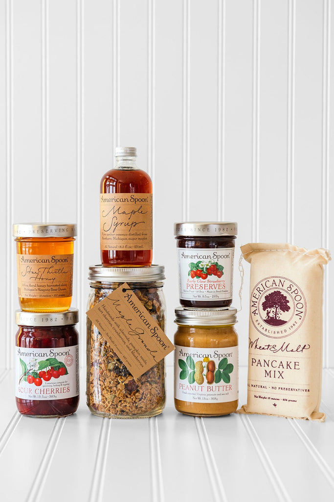 American Spoon products stacked together - Star Thistle Honey, Fruit Perfect Sour Cherries, Maple Granola, Maple Syrup, Early Glow Strawberry Preserves, Peanut Butter and Wheat & Malt Pancake Mix