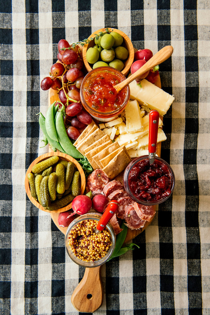 A charcuterie board with various meats, cheese, preserves, mustards and garnishes.