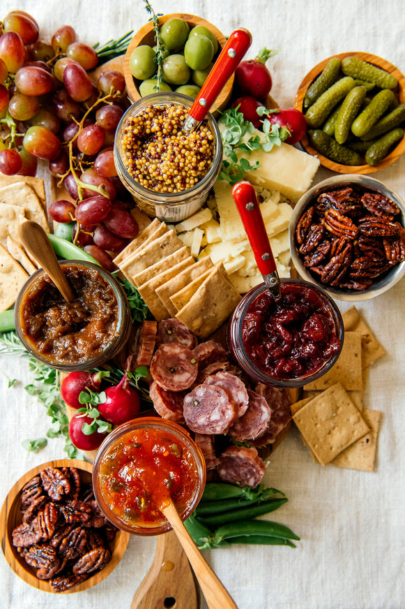 A charcuterie board with various meats, cheese, preserves, mustards and garnishes.