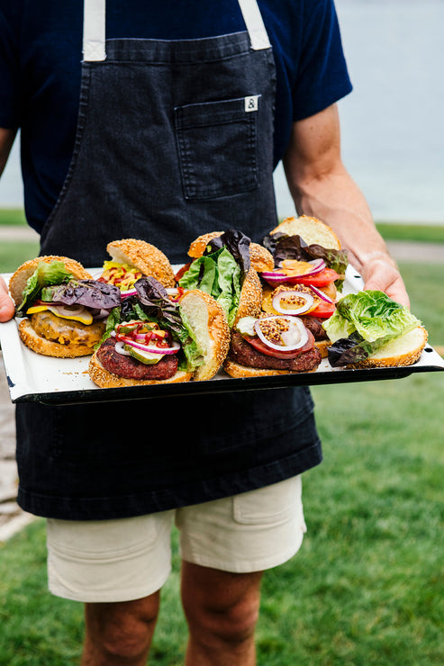 Load image into Gallery viewer, a man in an apron holding a platter of hamburgers