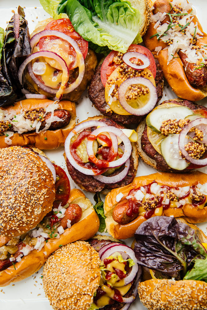 a platter of hamburgers and hot dogs with a variety of toppings