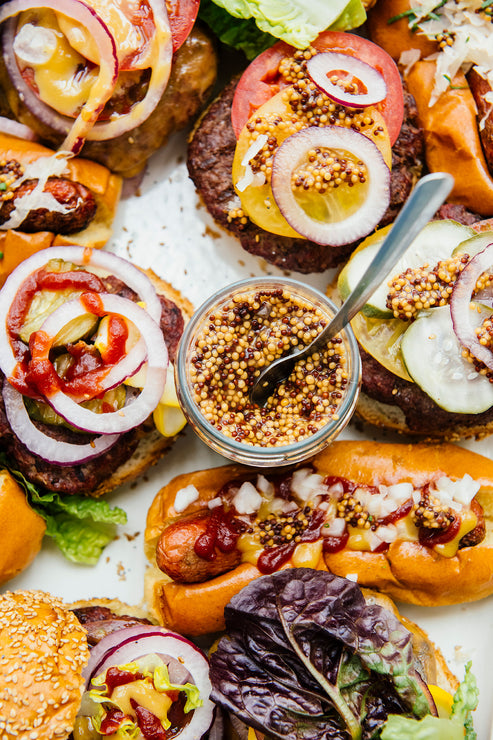 Load image into Gallery viewer, a platter of hamburgers and hot dogs with toppings and an open jar of whole seed mustard