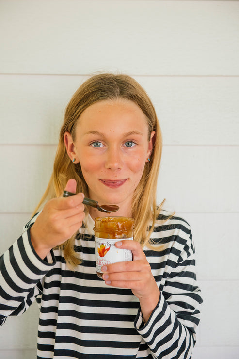 Load image into Gallery viewer, Young girl holding a jar of Salted Maple Caramel and a spoon against a white background