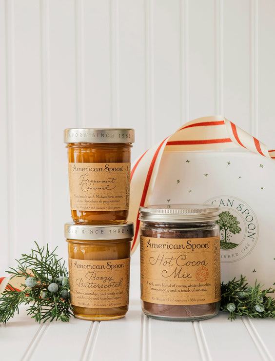 Load image into Gallery viewer, Three jars of American Spoon Hot Cocoa Mix, Boozy Butterscotch & Peppermint Caramel on a white surface with a decorative ribbon and greenery.