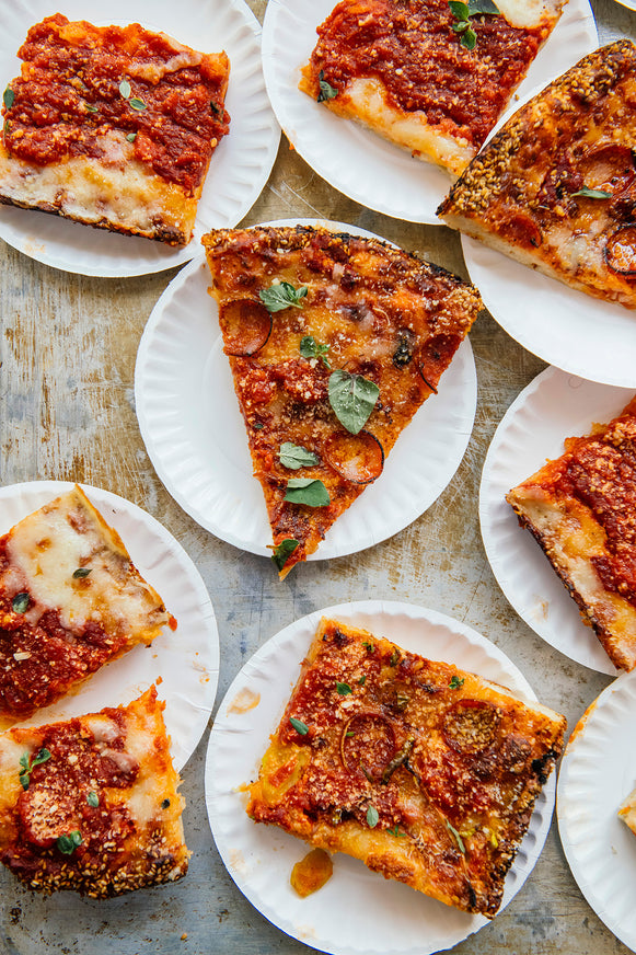 Multiple slices of pizza on paper plates arranged on a wooden table.