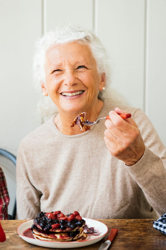 a woman eating a stack of pancakes topped with blueberries and cherries