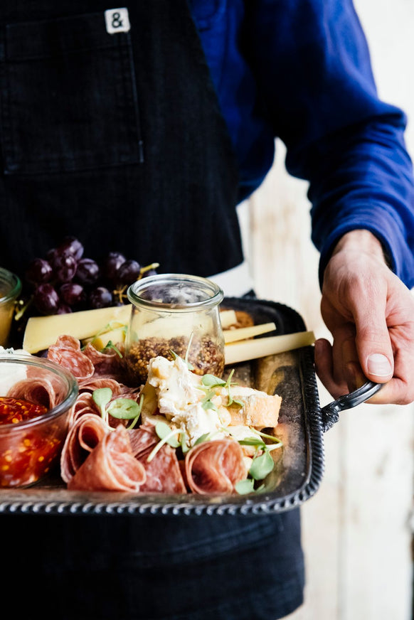 someone holding a charcuterie tray of meats, cheese and spread