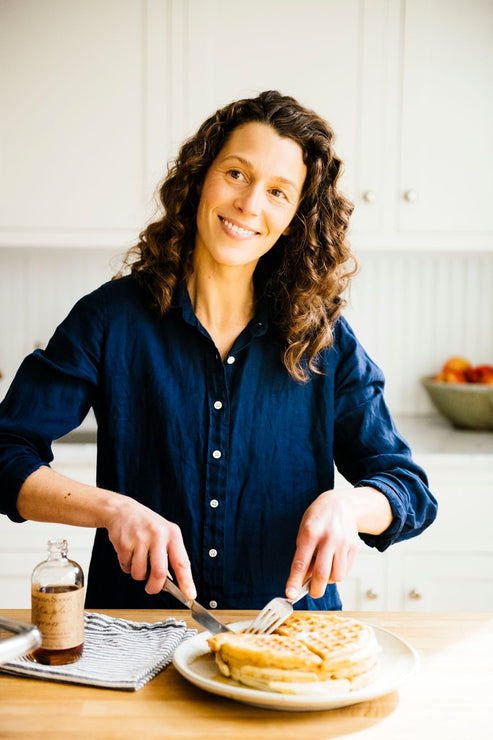 Load image into Gallery viewer, a woman cutting up a stack of waffles topped with maple syrup
