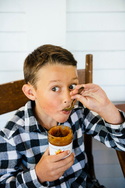 Load image into Gallery viewer, A young boy eating Salted Maple Caramel by the spoonful from the jar
