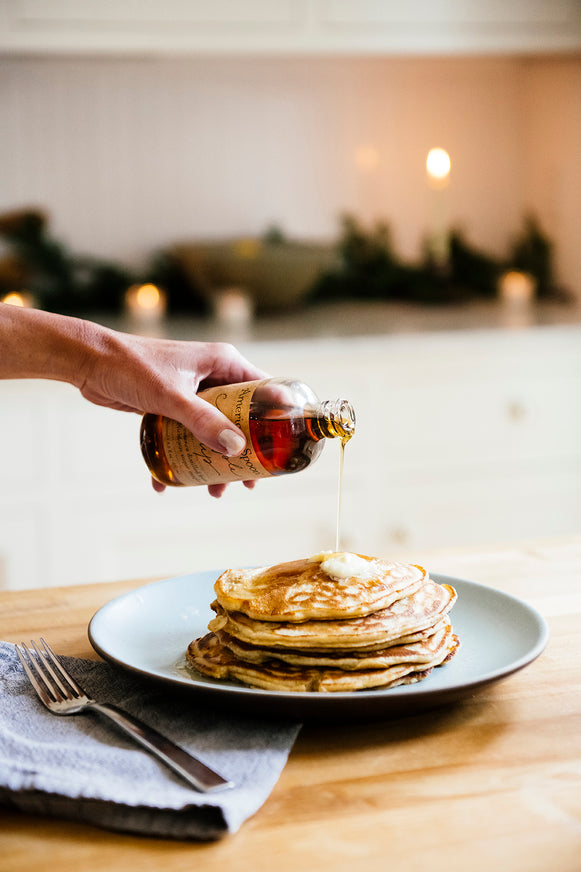 A stack of pancakes with melted butter and Maple Syrup drizzled over top