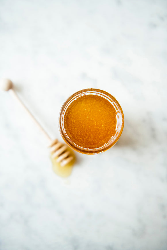 Birdseye view of a jar of Star Thistle Honey with a wooden honey dipper besides