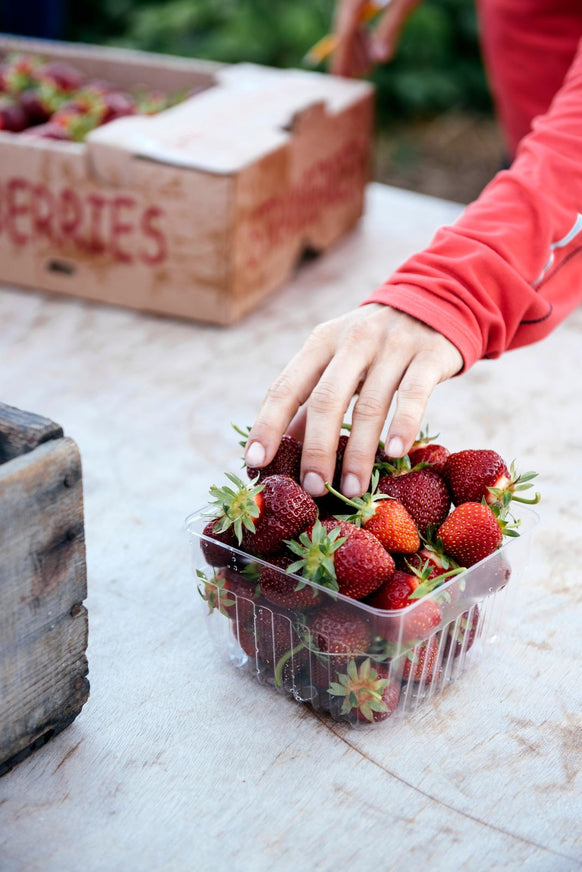 Customer reaching for fresh strawberries from a berry pint container