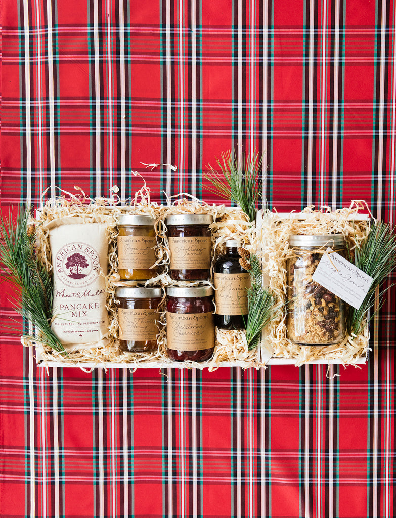 The Christmas Cheer gift box containing Wheat & Malt Pancake Mix, Peppermint Caramel, Holiday Jam, Star Thistle Honey, Christmas Cherries, Maple Syrup and Maple Granola surrounded by greenery