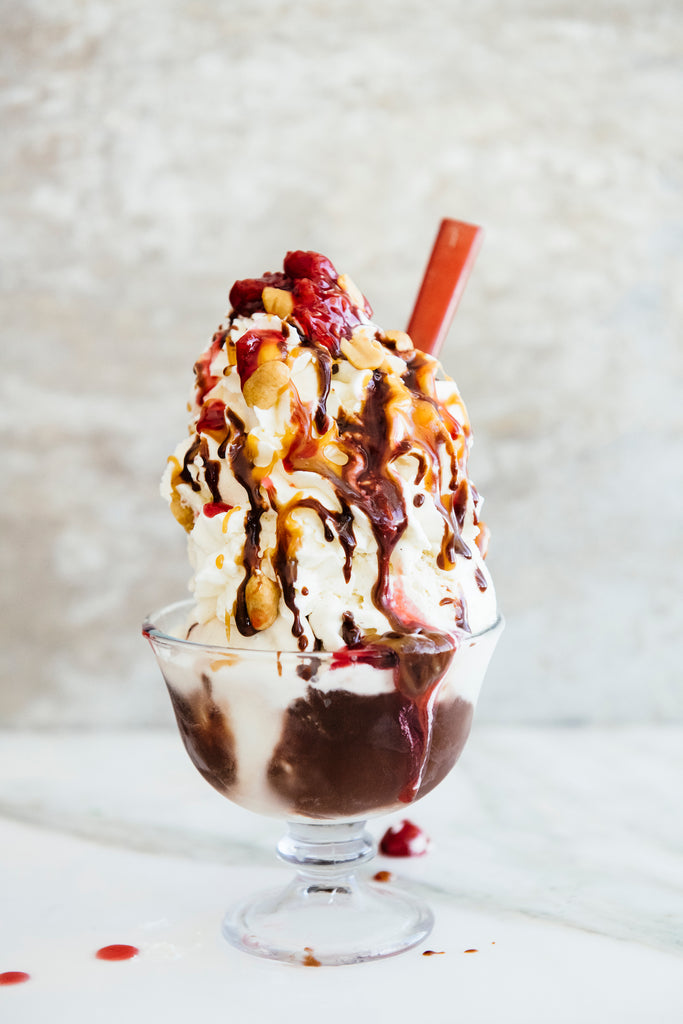 a bowl of ice cream topped with fudge sauce, caramel and cherries