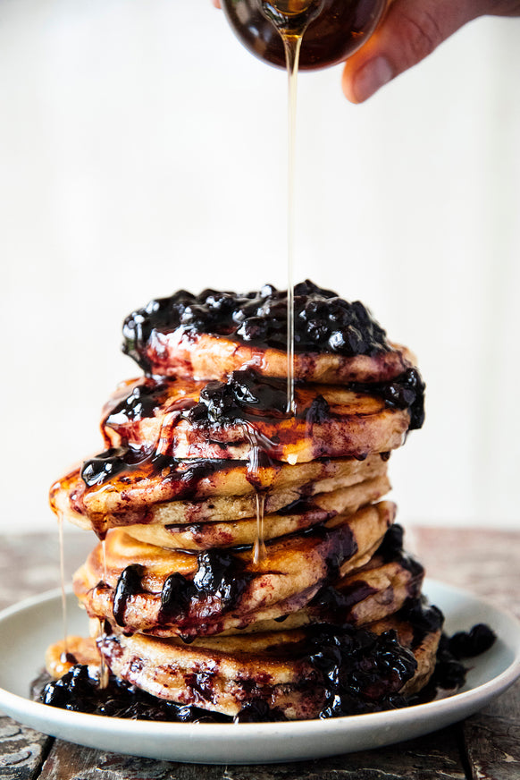 A tall stack of pancakes with Fruit Perfect Blueberries and maple syrup