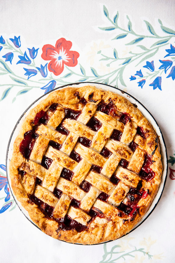 Cherry pie with a lattice crust on a serving plate with a flowered tablecloth.