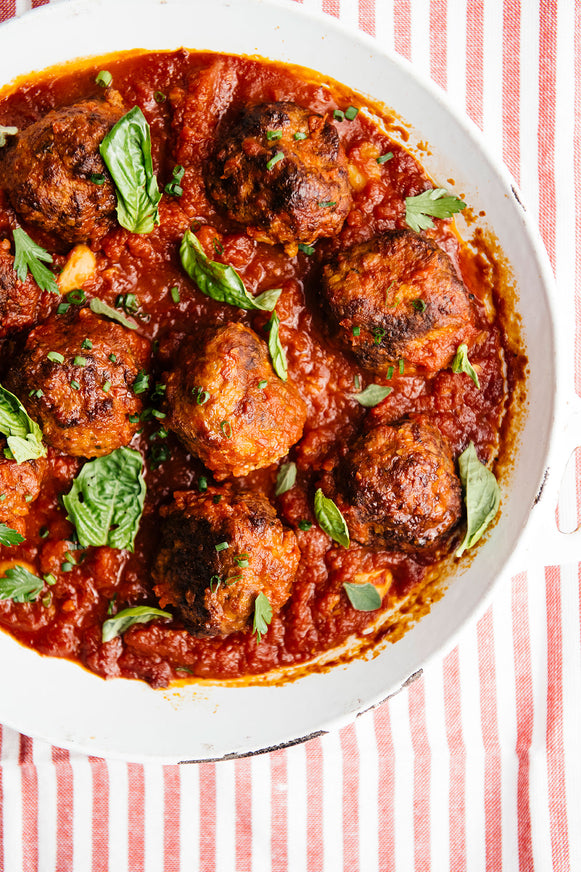 Large rustic bowl of meatballs and sauce sprinkled with fresh herbs